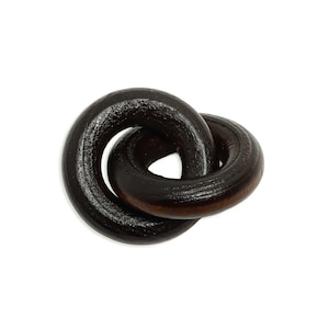 May include: A dark brown wooden decorative knot, featuring two intertwined circular loops. The wood grain is visible, adding texture to the piece. The knot is a symbol of connection and unity.