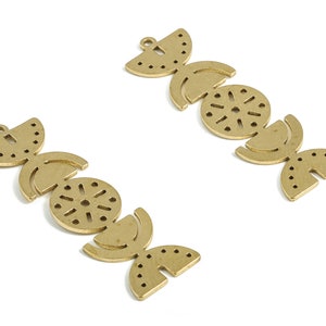 May include: Two gold-toned metal charms with geometric designs. Each charm features a series of interlocking circles, half-circles, and dots.