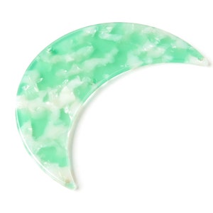 May include: A green and white marbled crescent moon shaped hair clip.