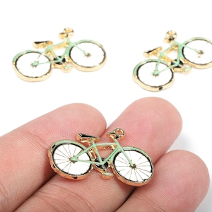 Könnte beinhalten: Goldfarbene Fahrradanhänger mit weißen Rädern und mintgrünen Rahmen. Die Anhänger sind mit Speichen und anderen Fahrradmerkmalen versehen. Drei Anhänger sind sichtbar, einer davon wird in einer Hand gehalten.