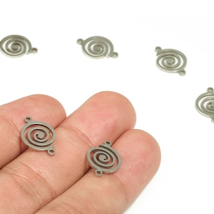 Puede incluir: Varios pequeños abalorios en espiral de color plateado, cada uno con dos agujeros para sujetar a la joyería. Los abalorios se muestran sobre un fondo blanco. Los abalorios metálicos presentan un detallado diseño en espiral.