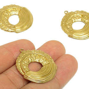 May include: Three gold-colored, circular jewelry pendants. Each pendant has a textured, ring-shaped outer edge and a smooth, curved section. A small loop is at the top for attaching to a chain or other jewelry component.