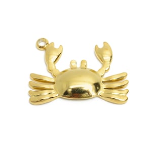 May include: A gold-coloured crab charm with a loop for attaching to jewellery or other crafts. The crab has detailed claws, legs, and a rounded body. The charm is set against a white background.