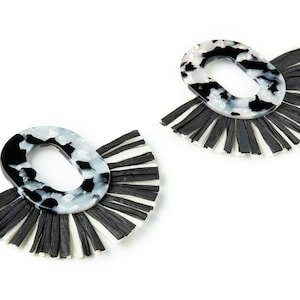 May include: A pair of black and white oval earrings with black and white fringe. The earrings are made of a marbled plastic material.