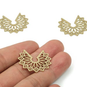 Puede incluir: Tres dijes de metal calado de color dorado, en forma de semicírculo, que se asemejan a un sol o un abanico. Los dijes se sostienen en una mano, mostrando su intrincado diseño simétrico. Ideales para la creación de joyas.