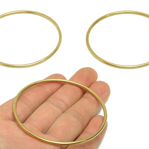Puede incluir: Tres brazaletes circulares de color dorado. Un brazalete se sostiene en una mano, mientras que los otros dos se muestran por separado. Los brazaletes están hechos de un metal fino y liso y tienen un acabado brillante. Los brazaletes tienen aproximadamente 7.6 cm de diámetro.