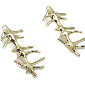 Puede incluir: Un par de pendientes de tono dorado con un diseño único, orgánico, con forma de rama. Los pendientes están hechos de metal y tienen un acabado brillante.