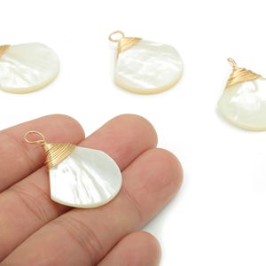May include: Four pearlescent, fan-shaped pendants with gold wire wrapping. One pendant is held in a hand. The pendants have a natural, iridescent sheen. These components are suitable for jewelry making, such as earrings or necklaces.