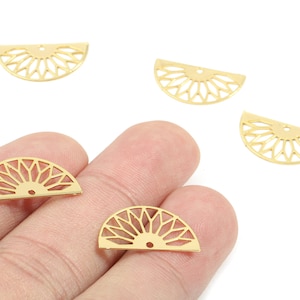 Pode incluir: Pingentes de metal dourado em forma de semicírculo com um desenho de explosão solar. Os pingentes têm um pequeno orifício na parte superior para enfiar. Vários pingentes estão espalhados em um fundo branco.