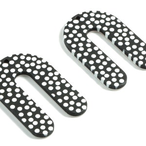 Könnte beinhalten: Zwei bogenförmige Ohrringe mit schwarzen und weißen Punkten. Die Ohrringe sind aus Holz und haben oben ein Loch zum Aufhängen.