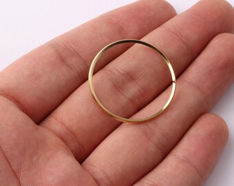 Może przedstawiać: Cienki, złoty metalowy pierścień o średnicy około 2,5 cm jest trzymany w otwartej dłoni osoby. Pierścień jest okrągły i wydaje się być biżuterią lub elementem większego przedmiotu.