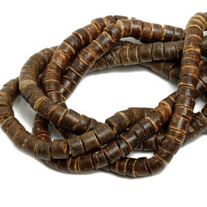 May include: A necklace of dark brown wooden beads, each cylindrical with a slightly textured surface. The beads are strung together, forming a coiled pattern against a white background. The beads appear to be approximately 1.3 cm in diameter.