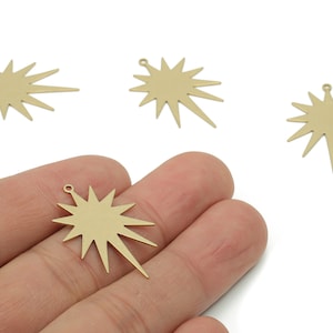 May include: Gold-colored starburst charms with a small loop at the top for jewelry making. The charms have a sunburst design with pointed rays. One charm is held in a hand, with others scattered around.