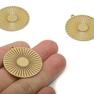May include: Three gold-coloured, circular pendants with a sunburst design. Each pendant has a small loop at the top for attaching to a chain or other jewellery component. The pendants are shown against a white background.