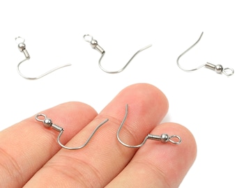 May include: Close-up of several silver-colored earring hooks. The hooks are in various stages of assembly, with some showing the full hook design and others partially formed. The hooks are held in a hand against a white background.