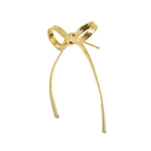 Puede incluir: Un lazo de metal dorado con colas largas. El lazo está hecho de un metal texturizado y tiene un diseño simple y elegante.
