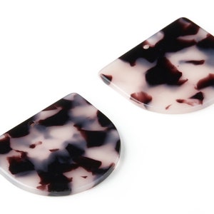 Puede incluir: Dos pendientes en forma de semicírculo con un patrón de mármol blanco, negro y marrón.