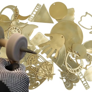 May include: A close-up of a variety of brass jewelry pieces, including a hand, a crescent moon, a butterfly, and a flower. The pieces are being polished with a buffing wheel.