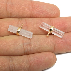 May include: Two clear quartz crystal pendants with gold-colored metal accents. Each crystal is rectangular and has a gold-colored band around the center with a small loop for hanging. The pendants are displayed on a hand.