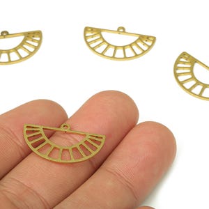 May include: Gold-colored metal charms in a half-circle sunburst design. The charms have a small loop at the top for attaching to jewelry. The image shows several charms, with one held in a hand.