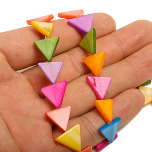 May include: A colorful necklace featuring triangular beads in various shades of pink, orange, yellow, green, purple, and blue. The beads are strung together, creating a vibrant and eye-catching accessory. The necklace is held in a hand.