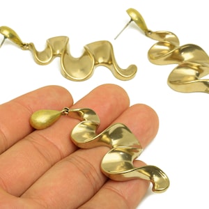 May include: Gold-toned, abstract earrings with a flowing, ribbon-like design. The earrings have a post-back closure and a teardrop-shaped accent. The jewelry is displayed on a white background.