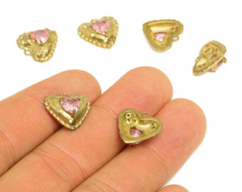 May include: Gold-toned heart-shaped charms with pink center stones and small clear accents. The charms have a textured border and a loop for attaching to jewelry. Several charms are scattered on a white background.