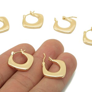 May include: Gold-coloured square hoop earrings. The earrings have a smooth, polished finish and a geometric design. Several earrings are displayed, with two held in a hand. The earrings are a classic jewellery item.