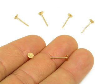 May include: Gold-colored earring posts with flat, round tops. Several posts are scattered on a white background, with one held between fingers. The posts are small, delicate, and suitable for jewelry making.
