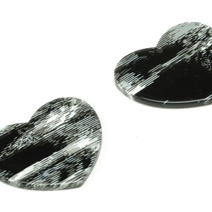 Może przedstawiać: Dwa sercowate elementy z żywicy z czarno-białym paskowanym wzorem.