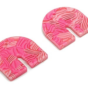 Könnte beinhalten: Zwei rosafarbene, bogenförmige Ohrringe aus Acryl mit einem Wirbelmuster.