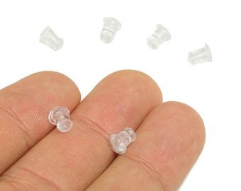 May include: A collection of clear, translucent earring backs. The earring backs are made of a soft, flexible material and are designed to secure earrings in place. Several are scattered on a white background.