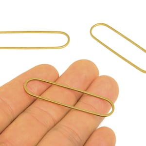 Può includere: Tre elementi di gioielleria in metallo dorato, ovali e allungati. Uno è tenuto in mano, mentre altri due sono posizionati su sfondo bianco. Questi elementi sono probabilmente utilizzati per la creazione di gioielli, come orecchini o pendenti.