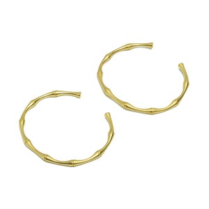 以下が含まれることがあります： 竹のデザインの金色のフープイヤリングのペア。イヤリングは金属製で、磨かれた仕上げになっています。