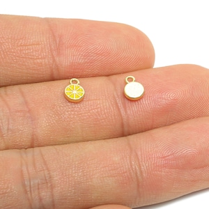 Może przedstawiać: Dwa małe, złote zawieszki. Jedna zawieszka to żółto-złota cząstka cytryny. Druga zawieszka to małe, złote kółko. Obie zawieszki mają małą pętelkę u góry do mocowania biżuterii.