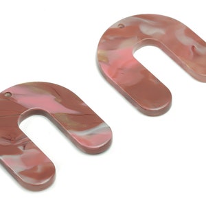 May include: Two U-shaped pendants with a marbled design. The pendants are primarily a reddish-brown color, with swirls of pink, white, and gold. Each pendant has a small hole at the top for stringing. The pendants are likely for jewelry making.