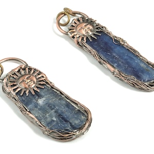 Può includere: Due ciondoli in cristallo di cianite blu avvolti in filo di rame. Ogni ciondolo presenta un ciondolo a forma di viso del sole con una finitura in rame.