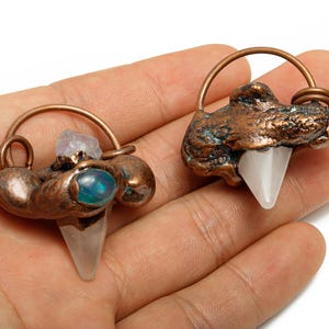 Könnte beinhalten: Zwei handgefertigte Kupferanhänger. Einer zeigt einen klaren Quarz-Kristall und einen blau-grünen Opal, der andere einen klaren Quarz-Kristall. Beide haben eine Kupferschlaufe. Schmuck.