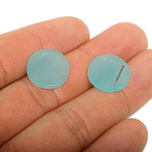 May include: Two round, light blue beads with a frosted appearance. One bead has a small hole, and the other has a silver-colored pin inserted. These beads are likely for jewelry making or crafting.