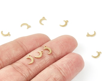 May include: Small, gold-colored crescent moon charms with a loop at the top for jewelry making. Several charms are scattered on a white surface, with some held between fingers. These charms are ideal for creating necklaces, earrings, and bracelets.