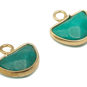 Può includere: Due ciondoli in pietra turchese con montature in metallo color oro e piccoli anelli per appenderli. I ciondoli hanno una superficie liscia e lucida e una forma arrotondata e irregolare. Le montature dorate aggiungono un tocco di eleganza.