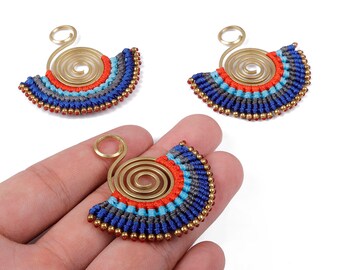 Könnte beinhalten: Drei handgefertigte fächerförmige Ohrringe. Jeder Ohrring hat eine Messingspirale und ein Makramee-Design in Blau, Grau, Rot und Gold. Die Ohrringe sind mit kleinen goldenen Perlen am unteren Rand verziert.