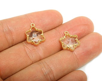 May include: Two star-shaped pendants with a clear, faceted center and a gold-colored, beaded frame. Each pendant has a small loop at the top for hanging. The pendants are displayed on a light-colored background.
