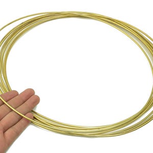 以下が含まれることがあります： 細い金色の金属リングのコレクション。ジュエリー作りや工芸品に使う可能性があります。リングは重ねられており、1つは手で持たれており、白い背景が使われています。