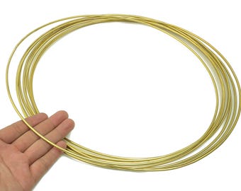 以下が含まれることがあります： 細い金色の金属リングのコレクション。ジュエリー作りや工芸品に使う可能性があります。リングは重ねられており、1つは手で持たれており、白い背景が使われています。