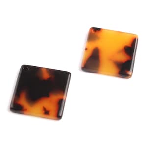 May include: Two square-shaped, brown and orange patterned resin embellishments with a hole at the top.