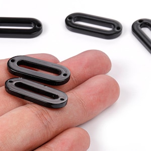 May include: Several black oval-shaped beads with two small holes on each end. The beads are glossy and appear to be made of a hard material. The beads are shown on a white background.