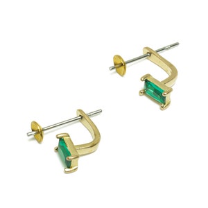 May include: A pair of gold-toned earrings with green rectangular gemstones. The earrings have a hinged back.