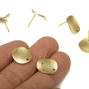 May include: A collection of gold-colored stud earrings in various organic shapes. The earrings have a brushed metal finish and include round, oval, and leaf-like designs. Some earrings are shown with their posts.
