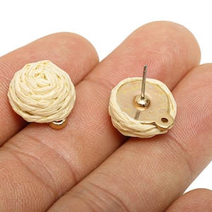 May include: Close-up of two beige woven stud earrings with gold-coloured posts and backing. The earrings are round, with a spiral design, and are set against a neutral background.